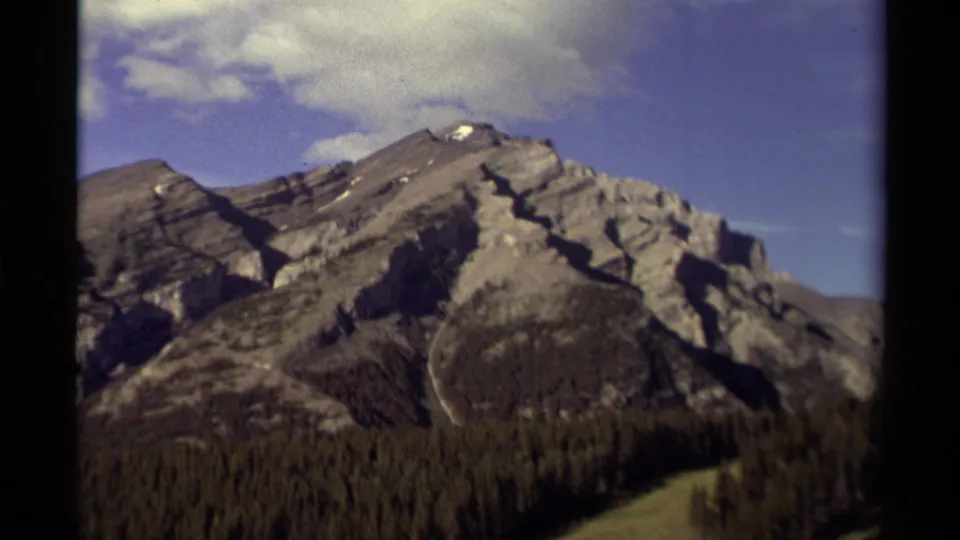 Final 1979 Canada 8mm frame showing a rugged mountain peak, small snow patches, forest below, and visible home-movie grain.