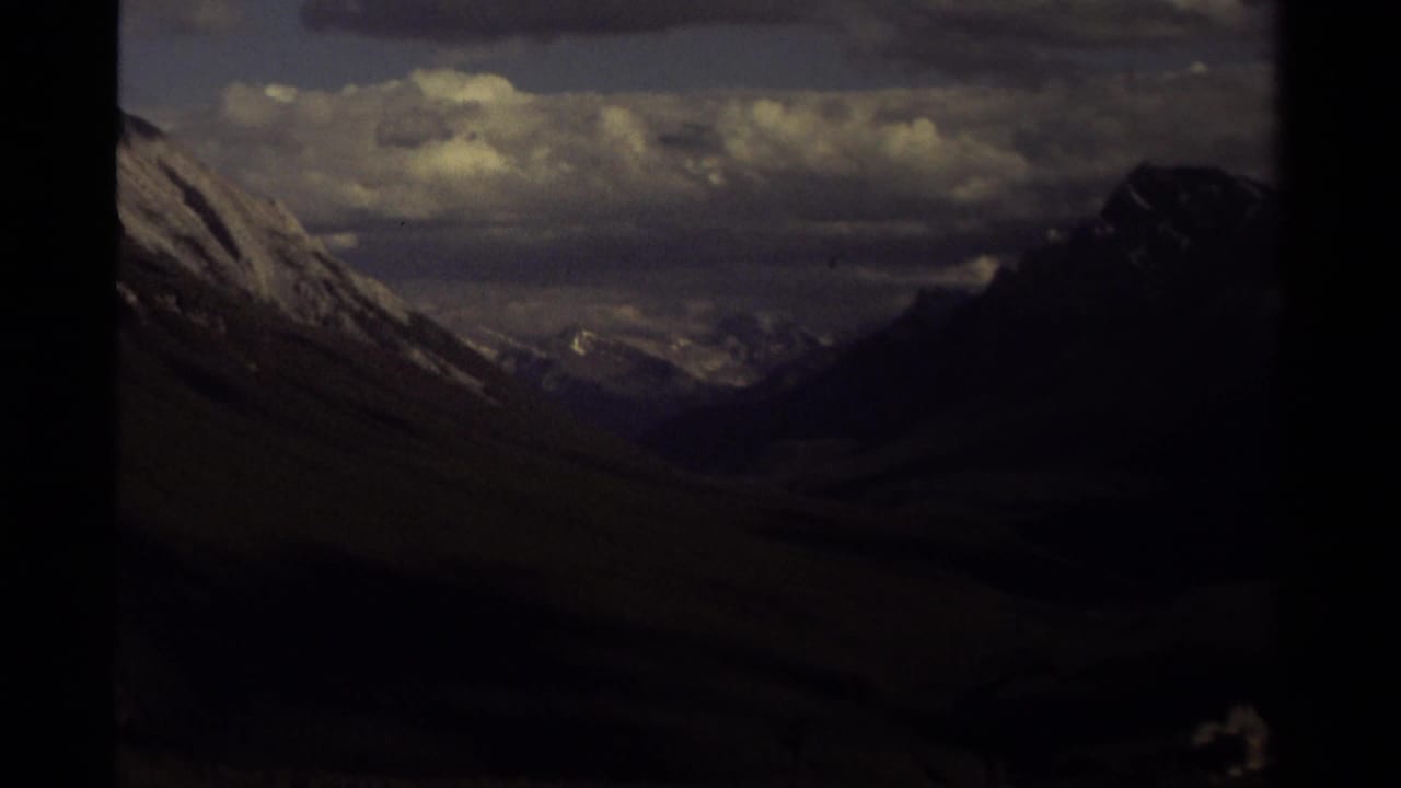 Dark mountain valley framed by steep snowy slopes under heavy cloud cover.