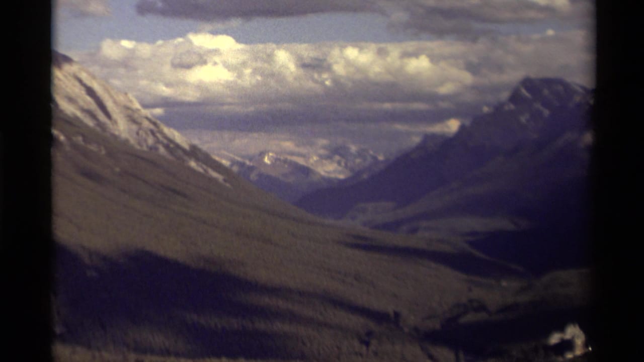 Mountain valley under a cloudy sky with snow-streaked slopes and dark 8mm frame edges.