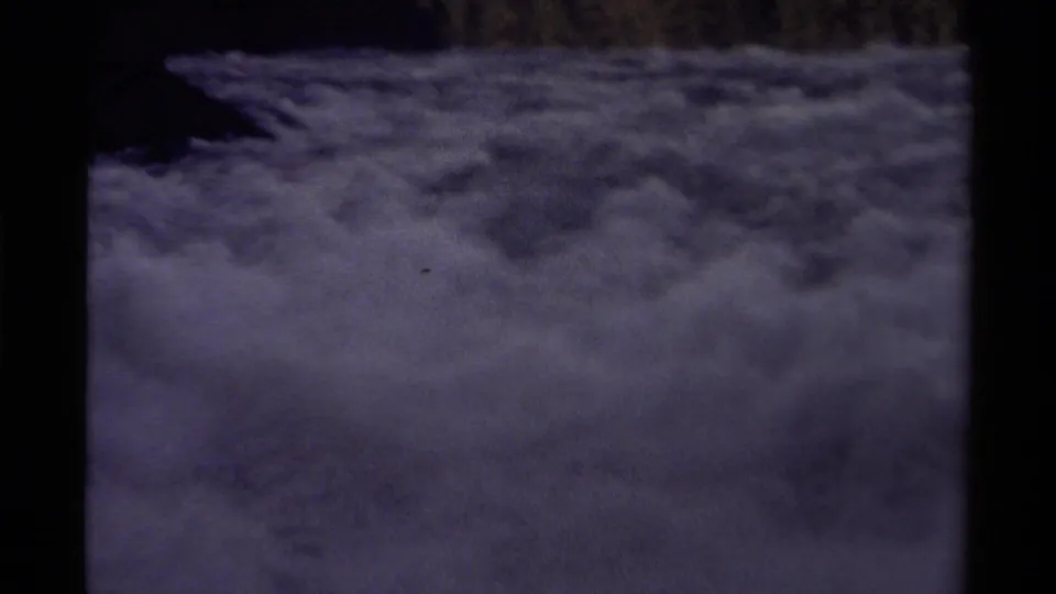 Soft 8mm frame from Canada in 1979 showing mist or low cloud over a valley, bordered by dark slopes and faint treetops.