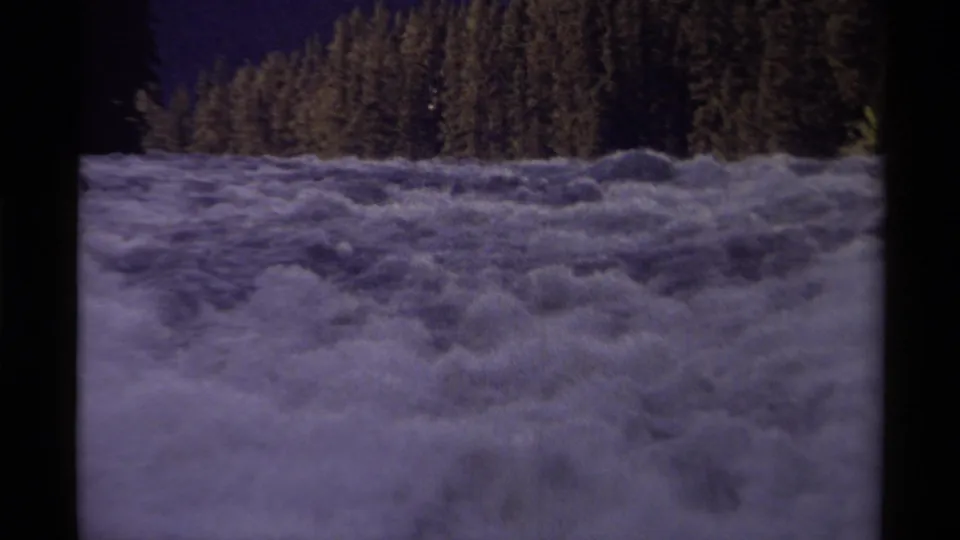 Close 1979 Canadian 8mm view of foaming river rapids with a dense evergreen bank in the background.