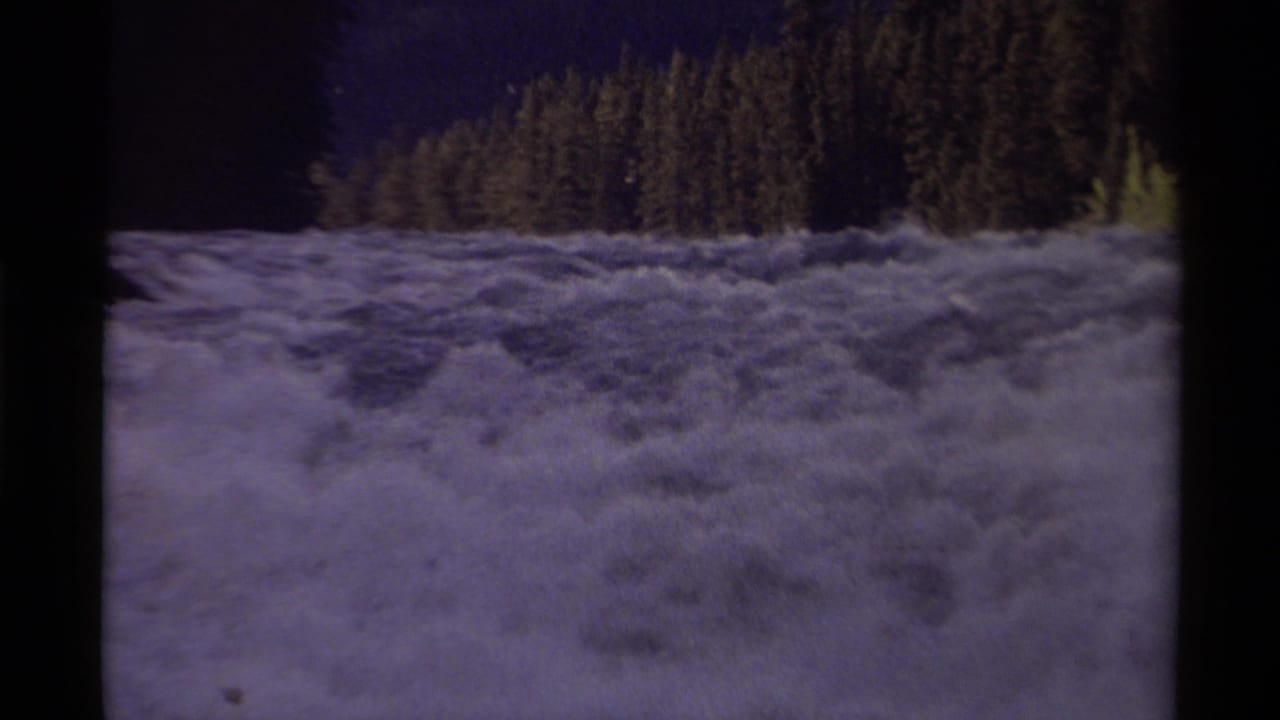 1979 8mm Canada footage showing turbulent white rapids with evergreen forest and shadowed hills beyond.