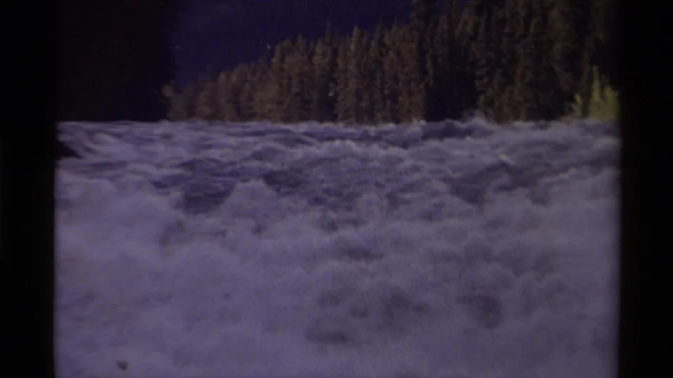 1979 8mm Canada footage showing turbulent white rapids with evergreen forest and shadowed hills beyond.