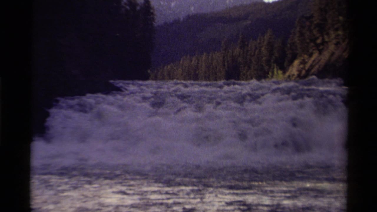 Foamy river rapids in Canada, filmed on 8mm in 1979, with dense trees and rugged hills behind the water.