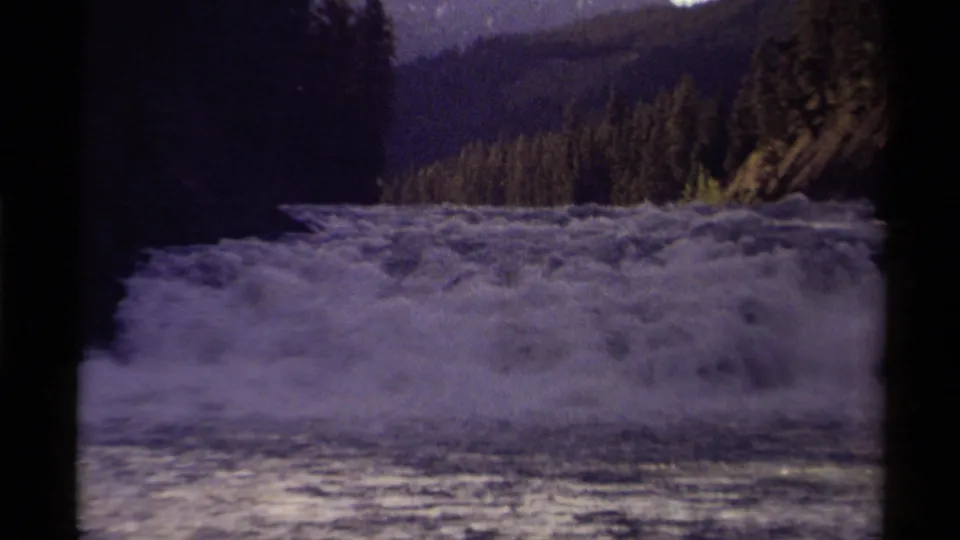 Foamy river rapids in Canada, filmed on 8mm in 1979, with dense trees and rugged hills behind the water.