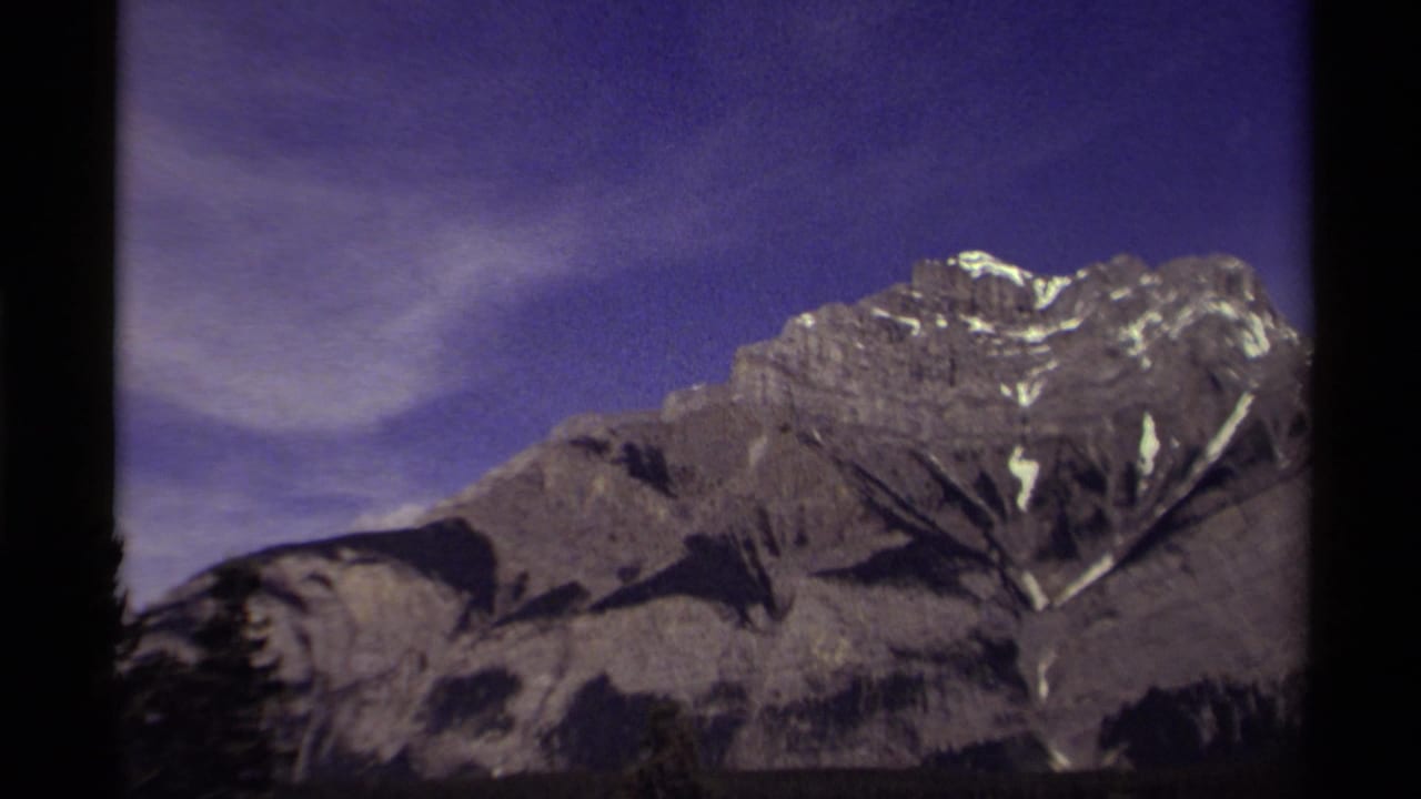 1979 Canadian 8mm frame of a rugged mountain peak with small snow patches against a blue-purple sky.