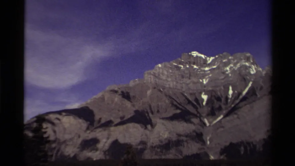 1979 Canadian 8mm frame showing a broad mountain face with snow traces, dark trees, and a blue-purple sky.