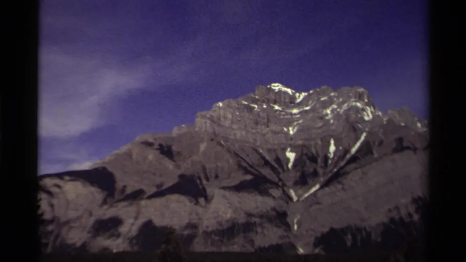 1979 Canadian 8mm frame of a mountain ridge with snow highlights and shadowed forest below.