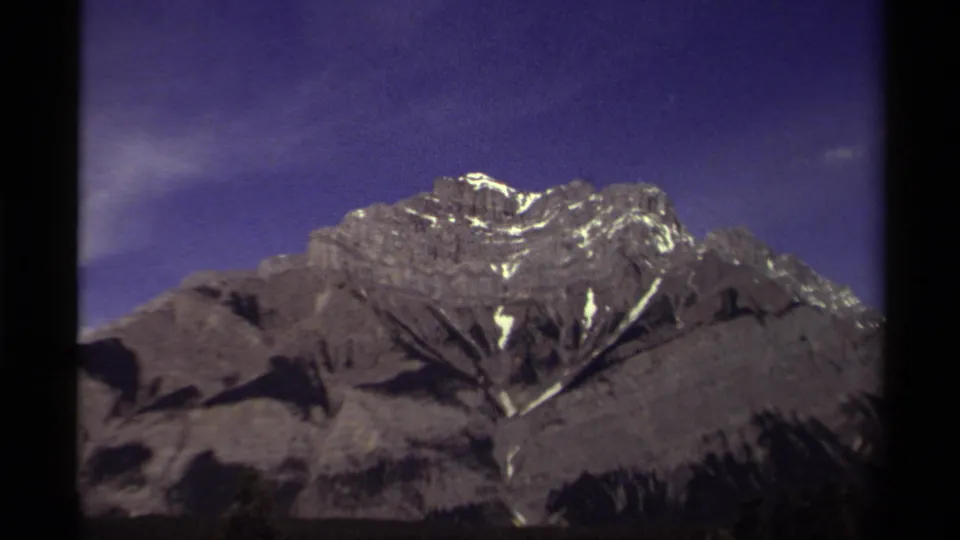 1979 Canadian 8mm view of rocky mountain peaks with bright snow patches and dark frame borders.