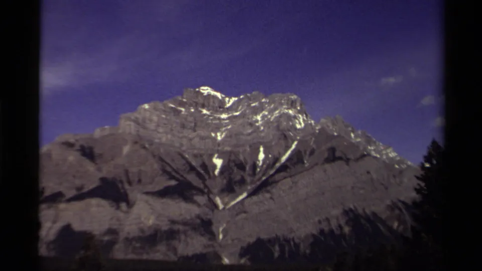 1979 Canadian home-movie frame of a mountain peak with snow streaks and silhouetted trees at the bottom.