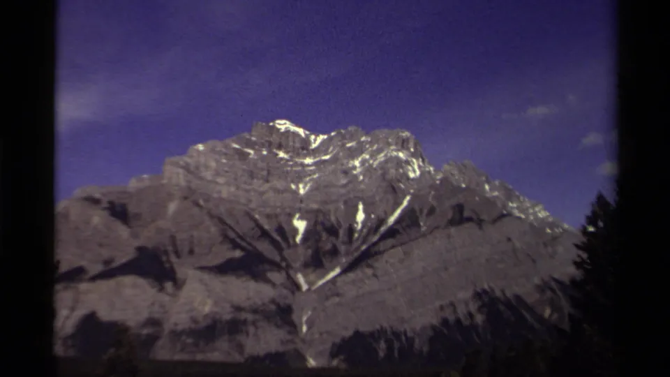 1979 Canadian 8mm frame showing a snow-capped ridge under purple sky, bordered by dark trees.