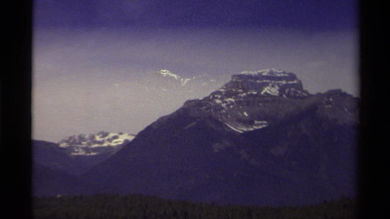 Snow-dusted mountain peak above a dark forest under a purple-gray sky.