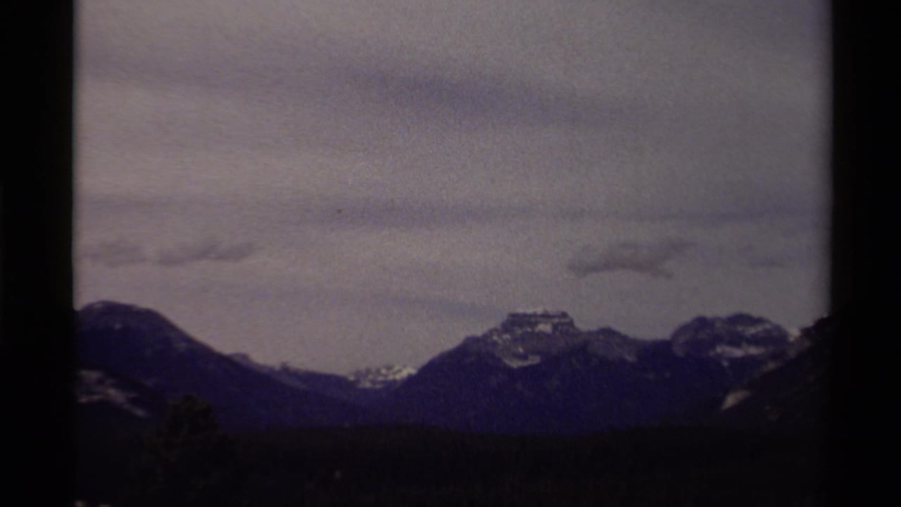 1979 Canadian 8mm frame showing distant mountains, snow patches, forested slopes, and an overcast sky.