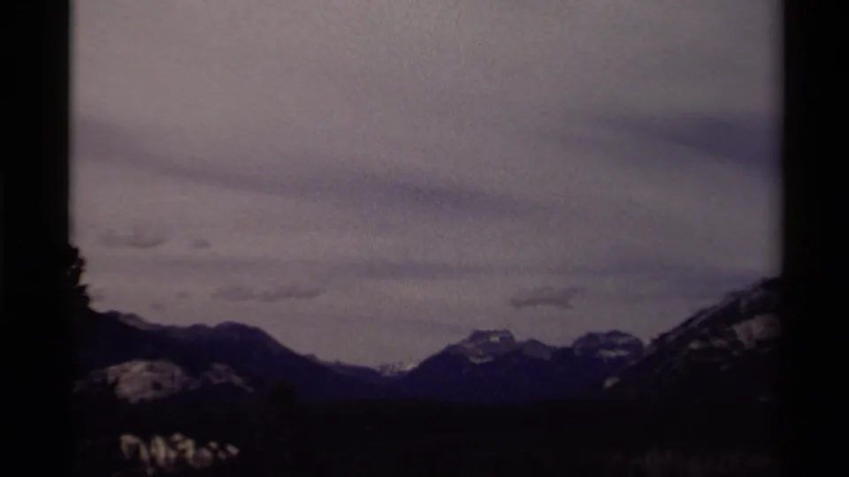 Canadian 1979 8mm frame showing a wide mountain horizon, dark wooded slopes, and layered clouds.