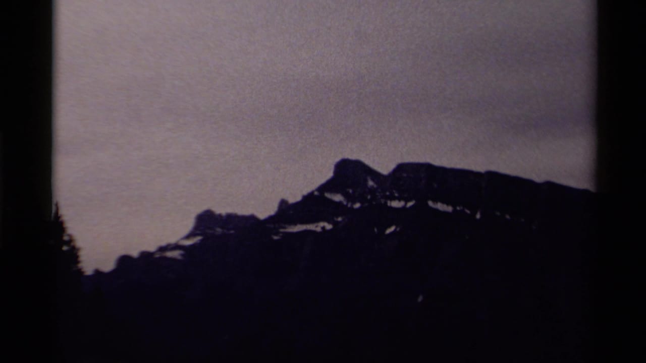 1979 Canadian 8mm frame showing a distant snow-patched mountain ridge beneath a muted gray sky with dark silhouetted foreground edges.