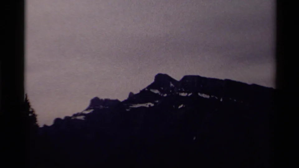 1979 Canadian 8mm frame showing a distant snow-patched mountain ridge beneath a muted gray sky with dark silhouetted foreground edges.