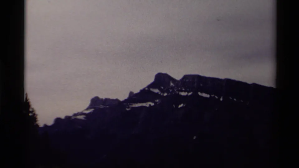 1979 Canadian 8mm view of a rugged mountain ridge with small snow fields, seen through soft focus and dark film-border framing.