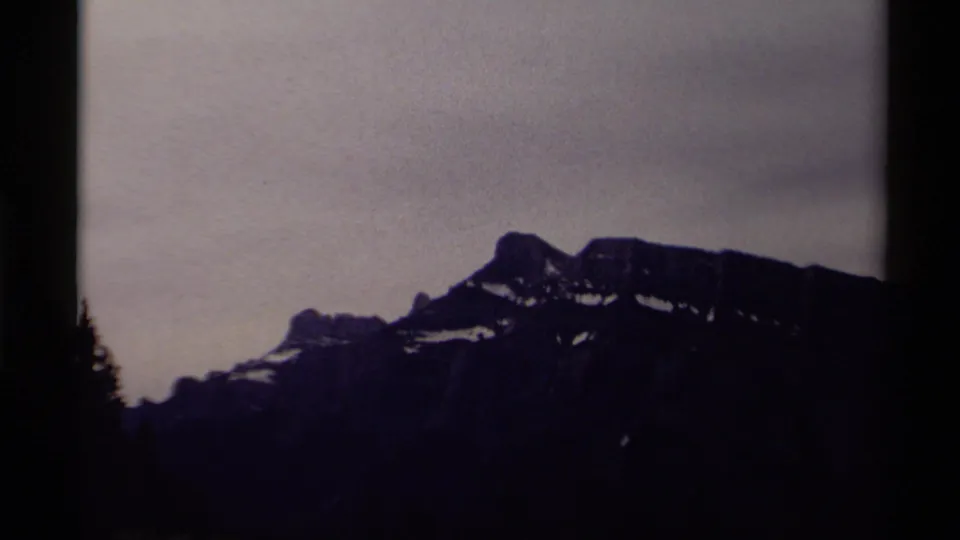 1979 Canadian home-movie frame of a distant snow-flecked mountain ridge under muted gray sky, with visible 8mm grain and dark borders.