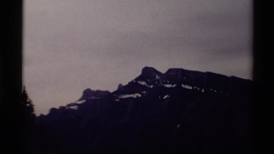 1979 Canadian 8mm frame showing a rugged snow-patched mountain silhouette under an overcast gray sky.