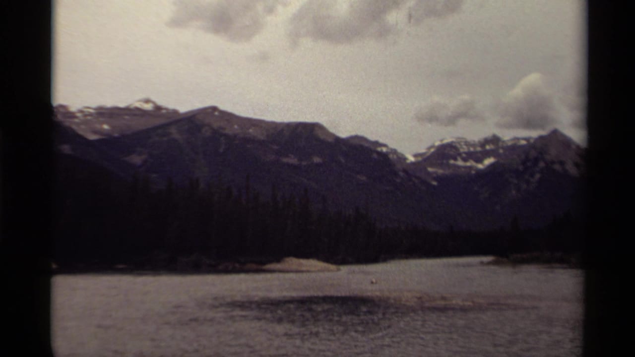 Mountain peaks and forested shoreline seen across a calm lake under clouds.