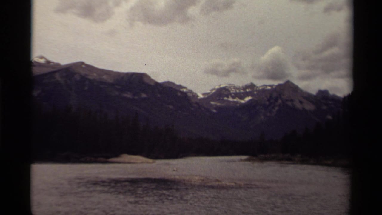 Canadian home-movie frame from 1979 showing a broad lake in front of dark mountain peaks and clouds.