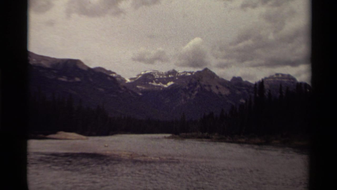 Mountain range, forested shoreline, and calm water beneath a gray clouded sky.