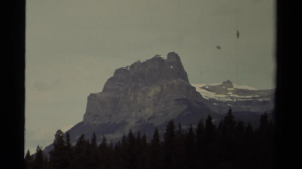 1979 Canada 8mm frame showing a rugged snow-dusted mountain above a dark spruce forest line beneath a cloudy sky.