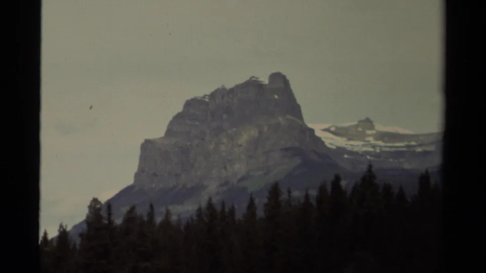 1979 Canadian 8mm frame holding on the mountain from a similar angle, with evergreen treetops across the lower frame.