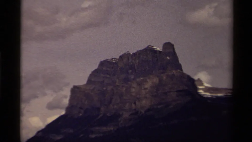 1979 Canadian 8mm frame of the mountain from a darker angle, with overcast sky and snow along the ridge.