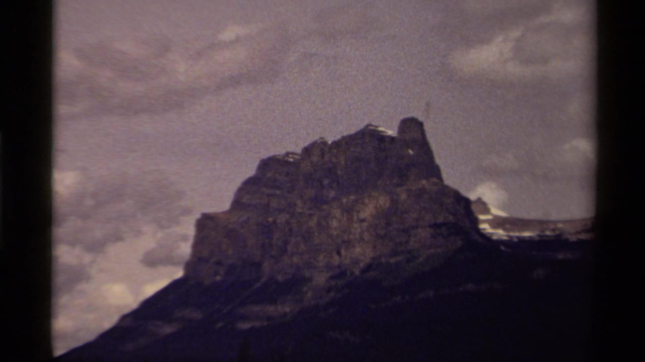 Rocky mountain peak under a cloudy sky, framed by dark film borders.