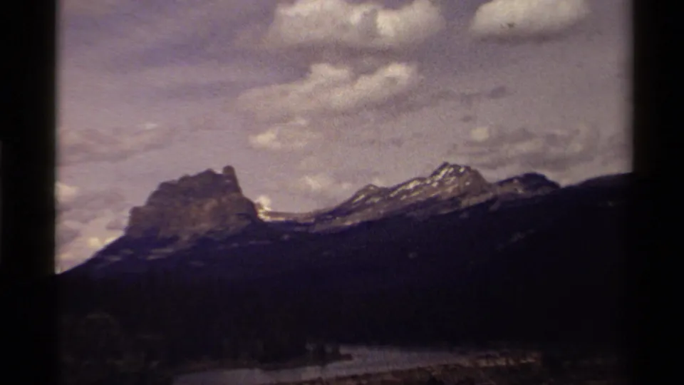 1979 Canadian 8mm view of a rocky mountain peak receding into ridges, with a lake or river visible below under scattered clouds.