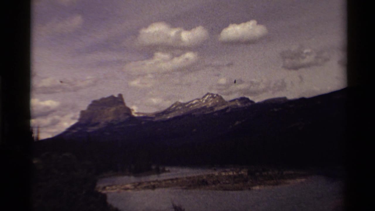 1979 Canadian 8mm view of rugged mountains above a broad waterway, with clouds and dark film-frame borders visible.