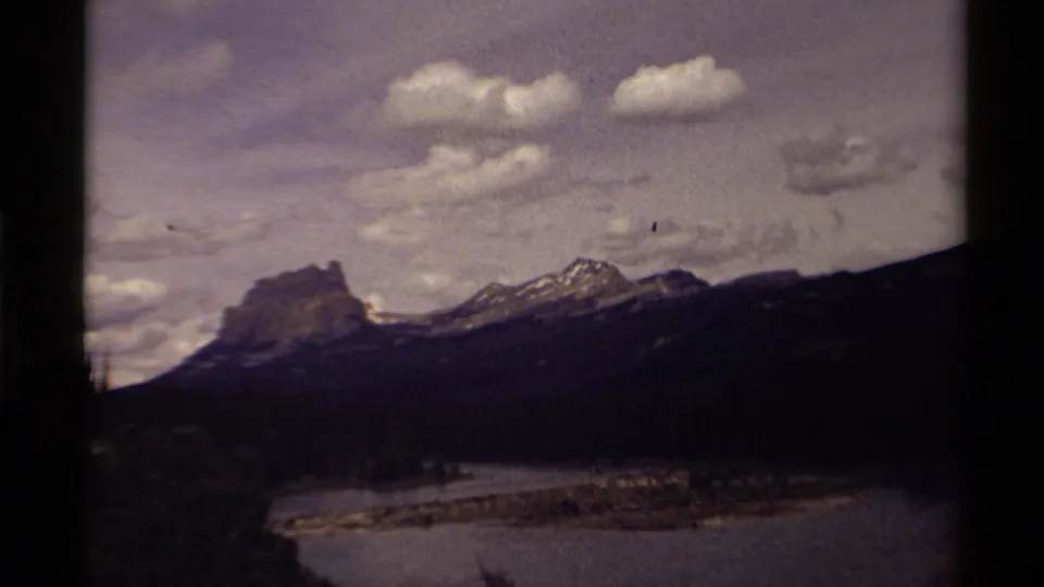 1979 Canadian 8mm view of rugged mountains above a broad waterway, with clouds and dark film-frame borders visible.