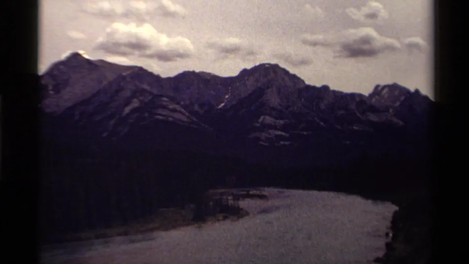 1979 Canadian 8mm frame showing a snow-streaked mountain ridge, forested slopes and a curving waterway in the valley.