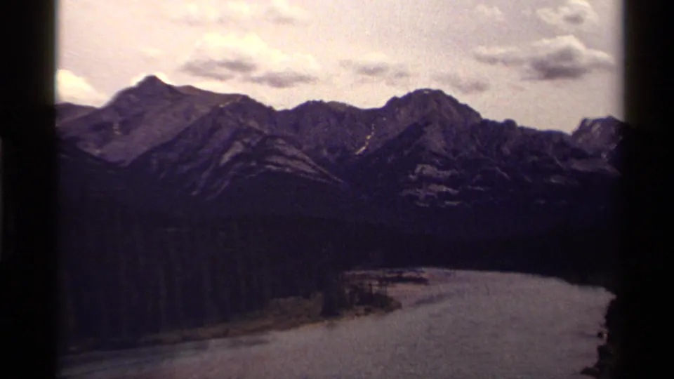 1979 Canadian 8mm landscape view of rugged mountains, a forested shoreline and a broad waterway framed by dark film edges.