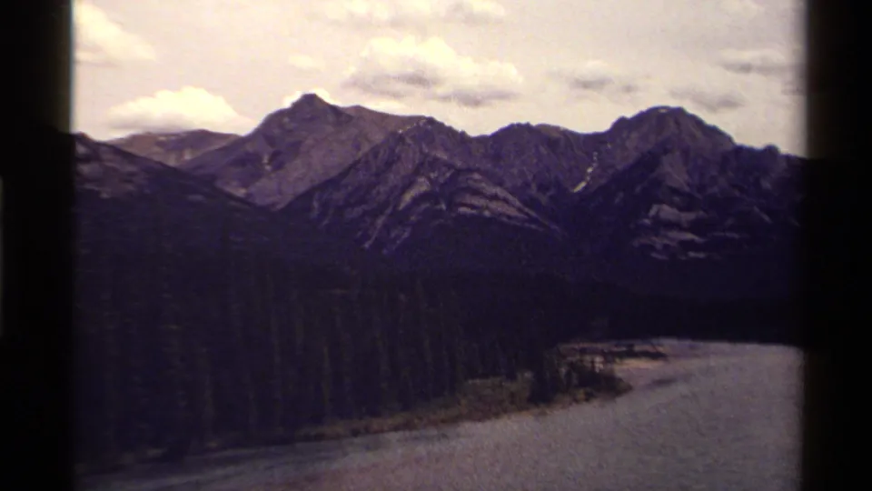 Faded 1979 Canadian 8mm landscape frame showing mountains, forested valley, and water under a pale cloudy sky.