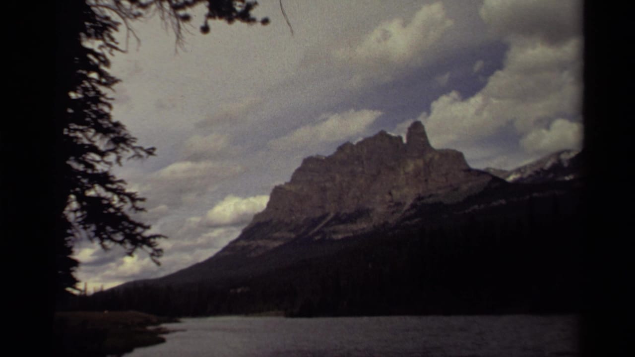 1979 Canadian 8mm landscape view of a rugged mountain rising beyond a lake, with evergreen branches at the frame edge.