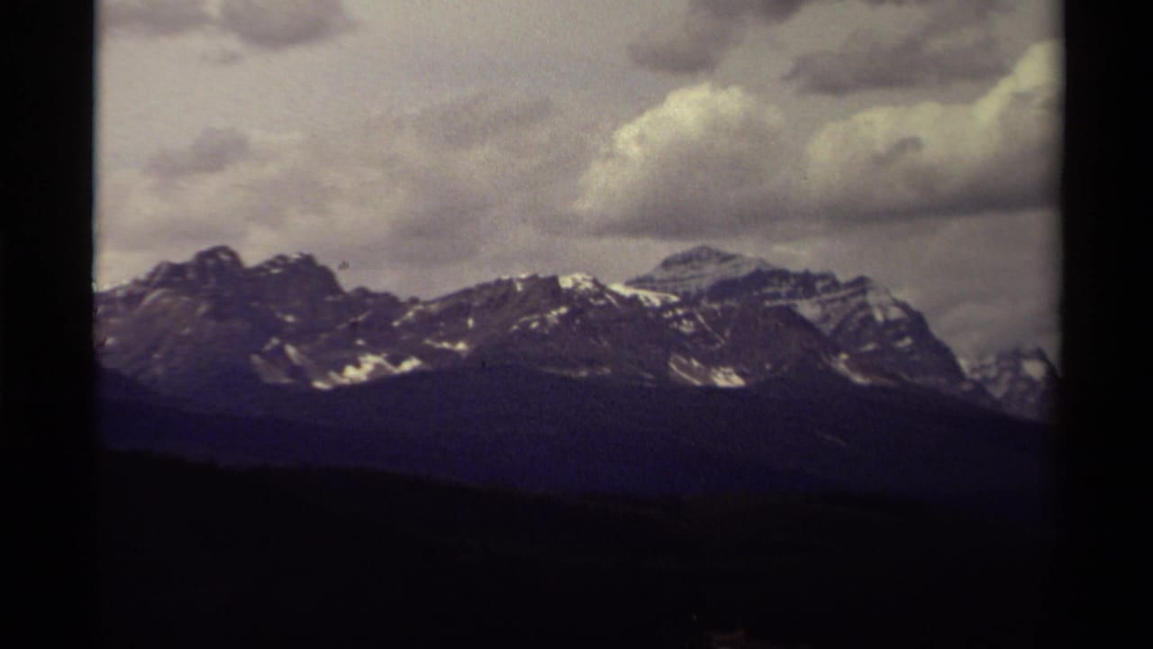 1979 Canadian 8mm frame of distant snow-streaked peaks beneath heavy clouds, partly divided by a dark film-frame edge.
