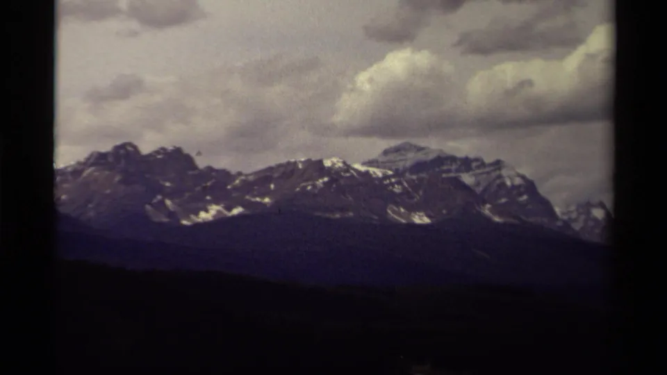 1979 Canadian 8mm frame of distant snow-streaked peaks beneath heavy clouds, partly divided by a dark film-frame edge.
