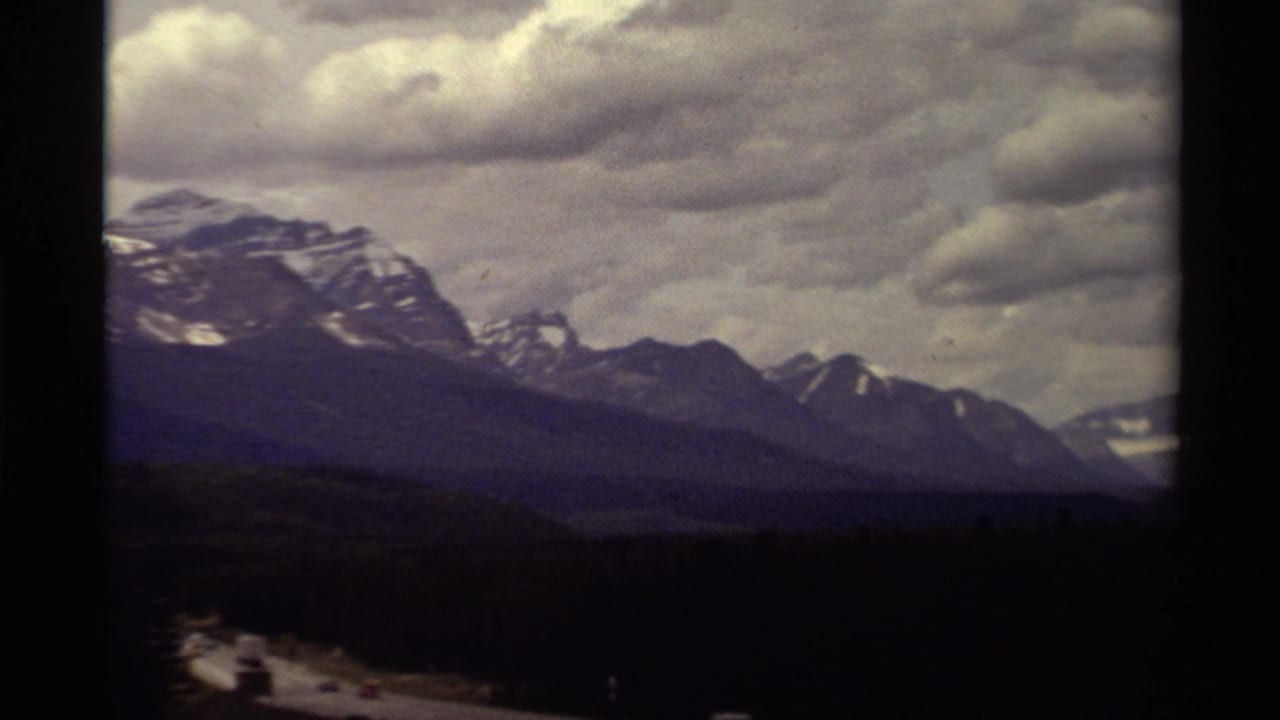 1979 Canadian 8mm view of rugged mountain ridges, snow patches, and a dramatic gray cloud layer over shadowed terrain.