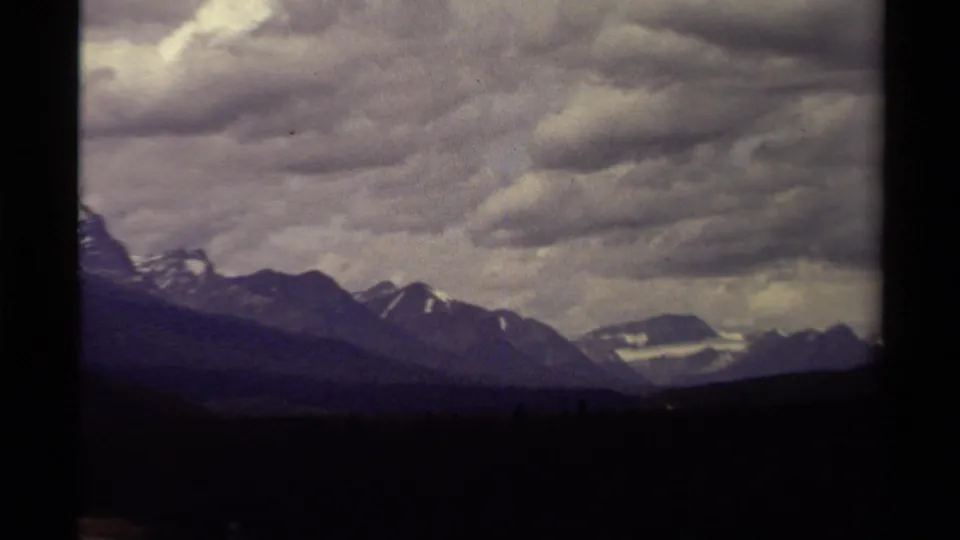 1979 Canadian 8mm frame with a cropped mountain ridge, distant snow patches, and a broad sky filled with textured clouds.
