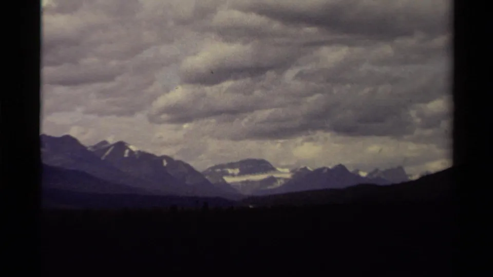 1979 Canadian 8mm twilight view of distant snowy peaks under layered gray clouds, with the foreground in deep shadow.