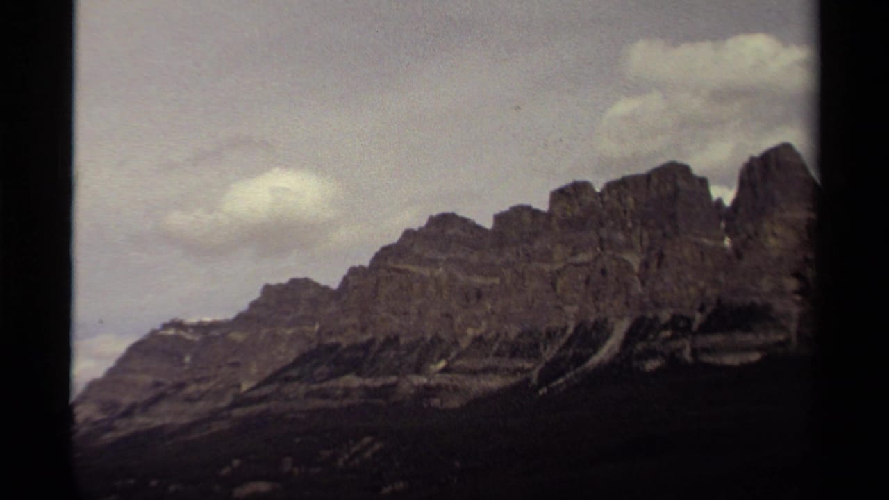1979 Canada 8mm view of a rugged mountain range under pale clouds, with soft focus, grain, and dark film borders.