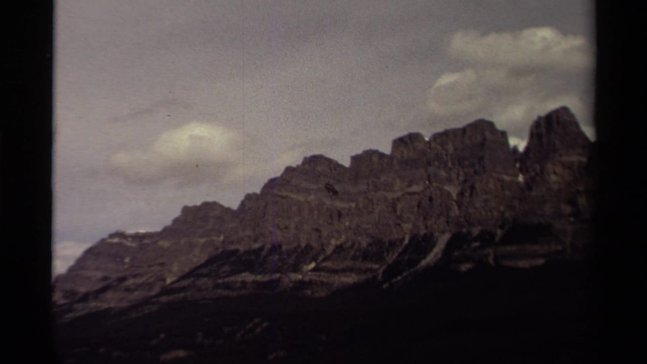 1979 Canada 8mm frame showing jagged mountain peaks and a soft cloud layer, with visible grain and dark edge framing.