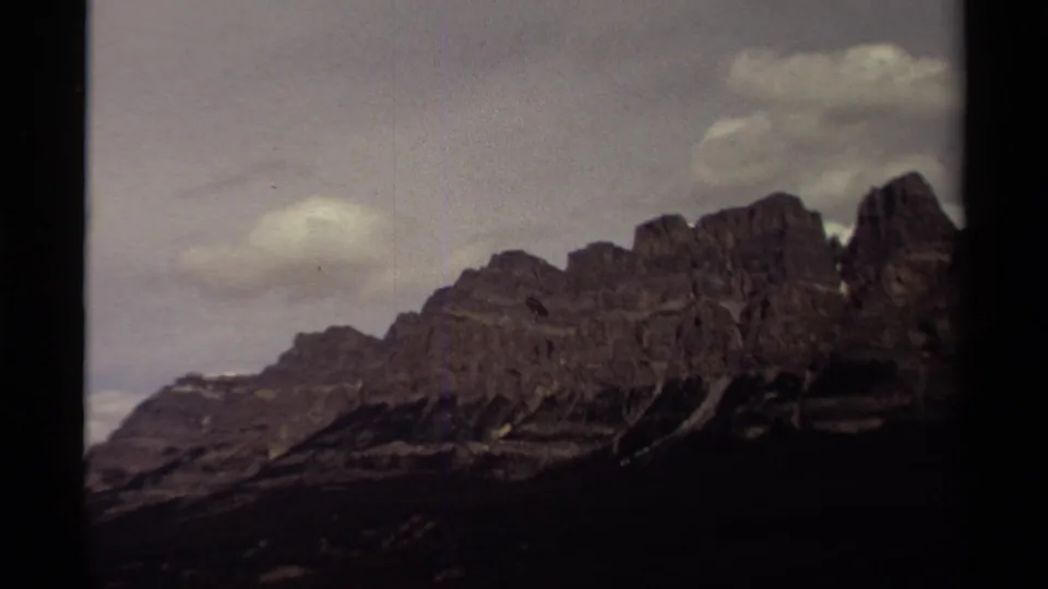 1979 Canada 8mm frame showing jagged mountain peaks and a soft cloud layer, with visible grain and dark edge framing.
