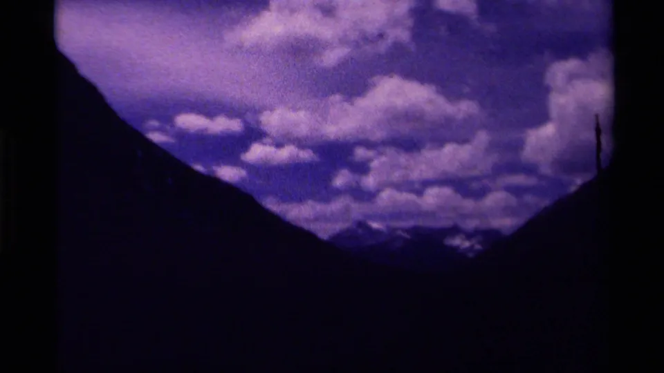 1979 Canada 8mm frame with dark mountain slopes, distant snowy peaks, and bright clouds across a blue-purple sky.