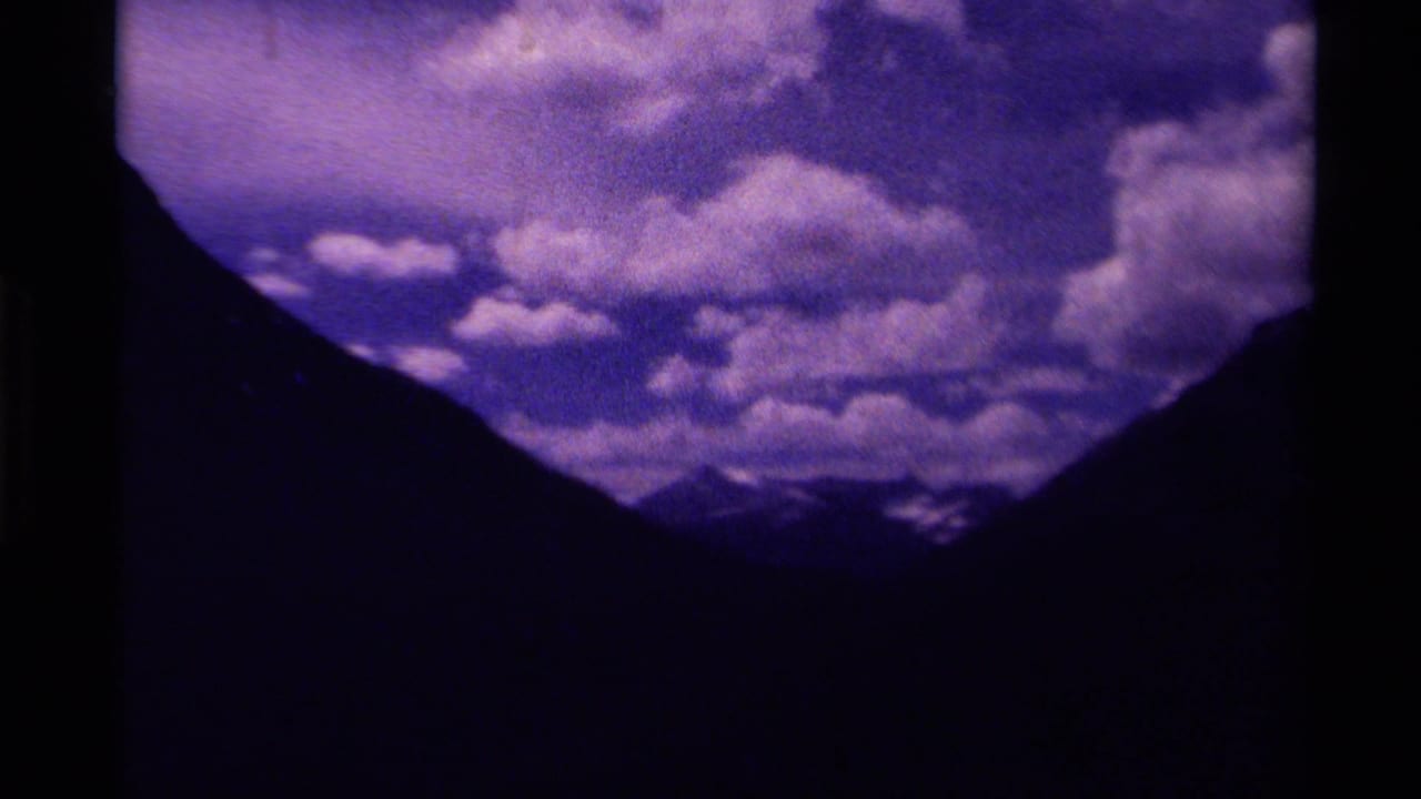 1979 Canada 8mm frame showing dark mountain slopes, distant snow-capped peaks, and a purple-blue cloudy sky.
