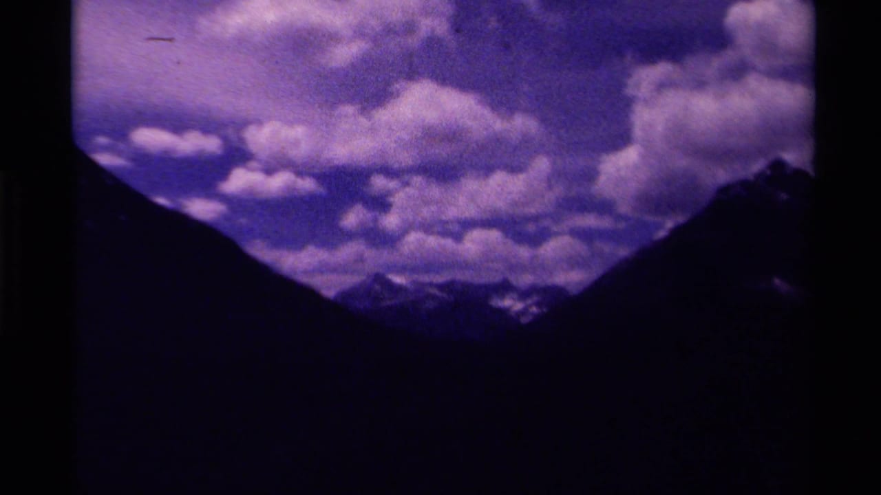 1979 Canada 8mm frame with a cloudy mountain valley, dark slopes on both sides, and distant snowy peaks under a cool color cast.