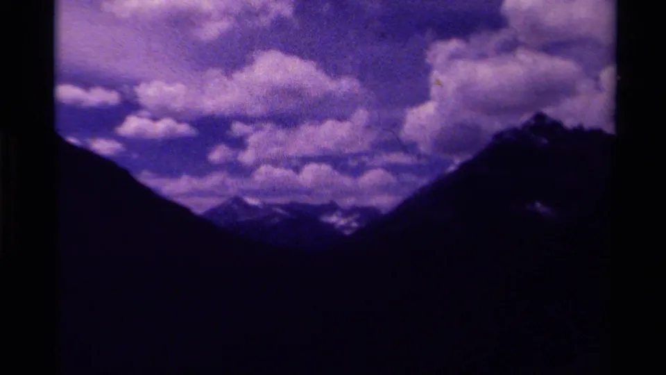 1979 Canada 8mm frame showing large bright clouds, dark mountain edges, and a distant valley with snow-touched peaks.
