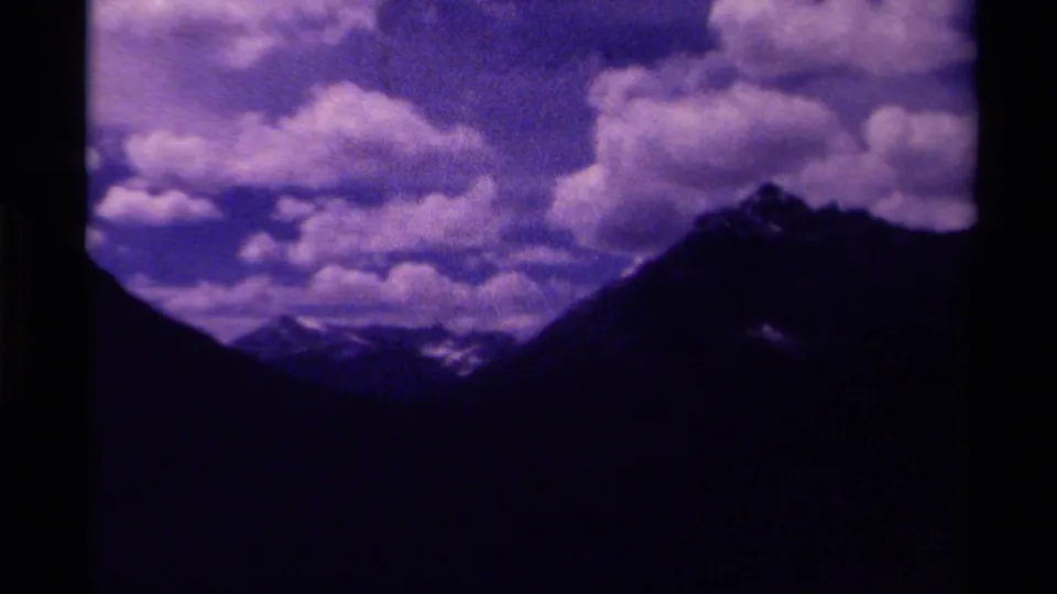 1979 Canada 8mm frame showing a broad cloudy sky above dark mountain silhouettes and distant snow-capped peaks.